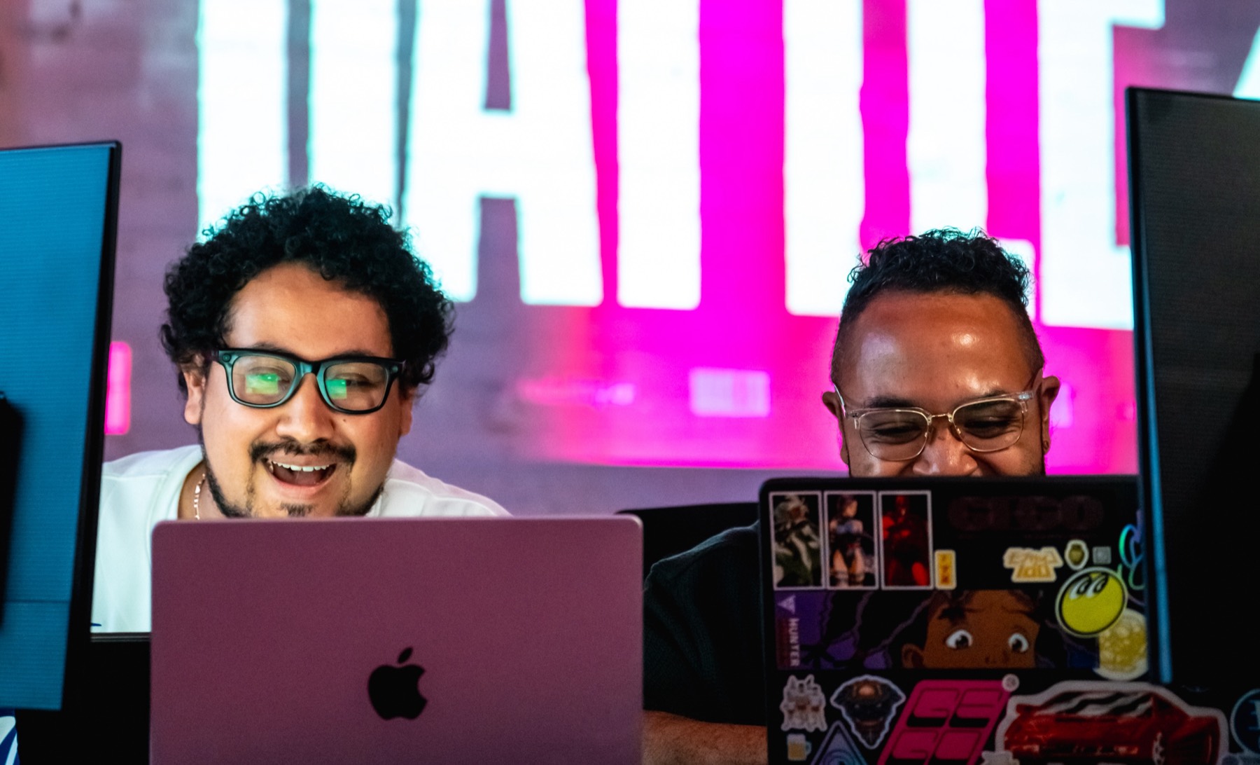 Two competitors laughing over their laptops under a glowing BATTLE sign at MAKE.EXE 2025