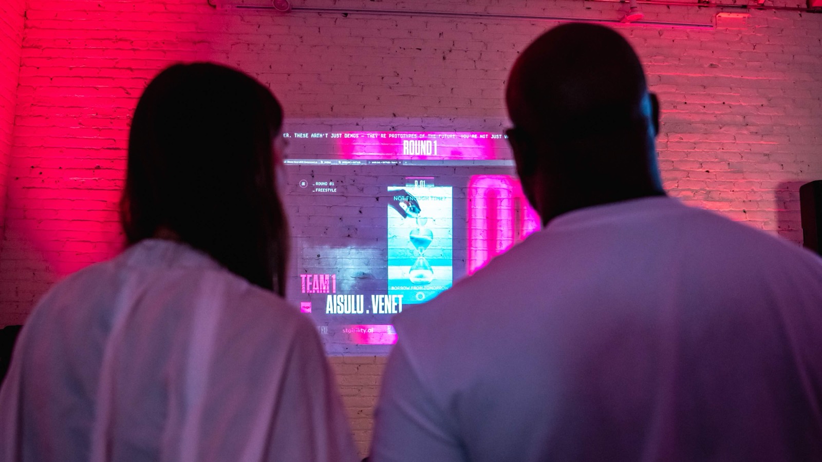 Two jurors seen from behind, watching Team 1's work go up on the screen in Round 1