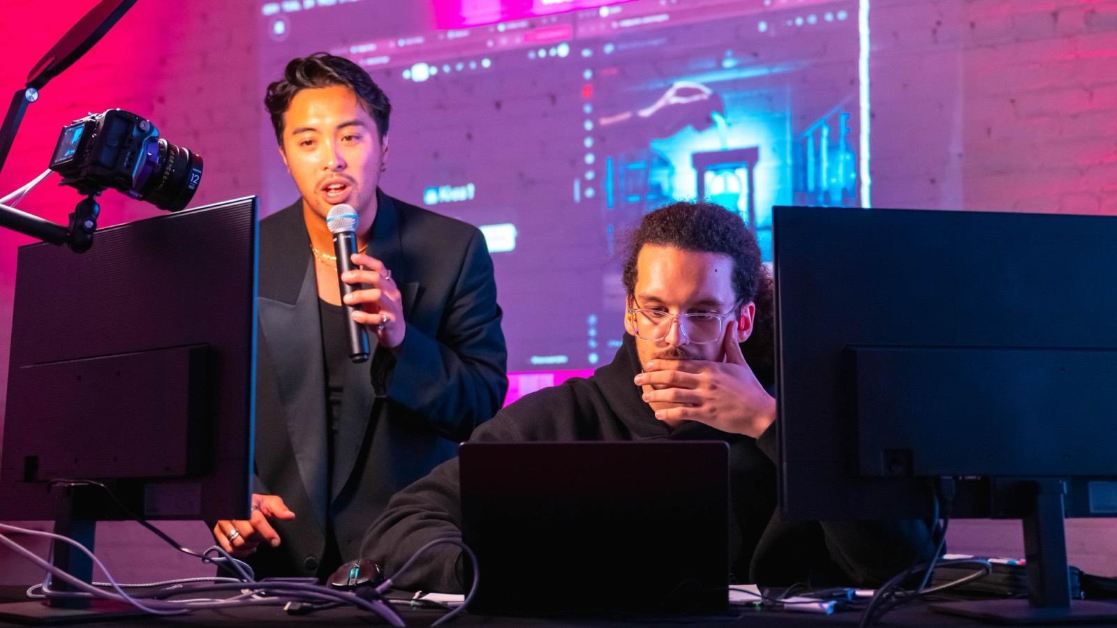 The MC on the microphone beside a competitor deep in concentration at his screen